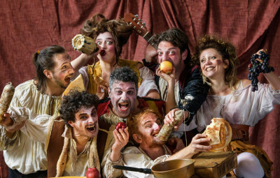 Gli interpreti di Stivalaccio Teatro in abiti di scena, ognuno intento a mangiare o bere qualcosa
