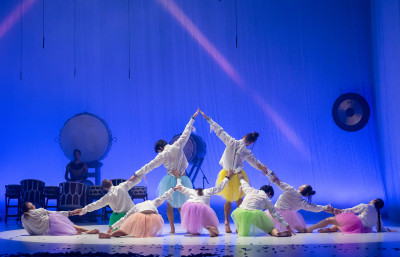 Danzatori in camicia bianca e gonne di tulle colorate posizionati a formare una forma di vulcano, nello sfondo i taiko giapponesi