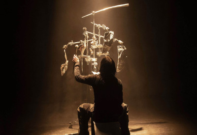 Performer di spalle suona uno strumento di sua creazione 